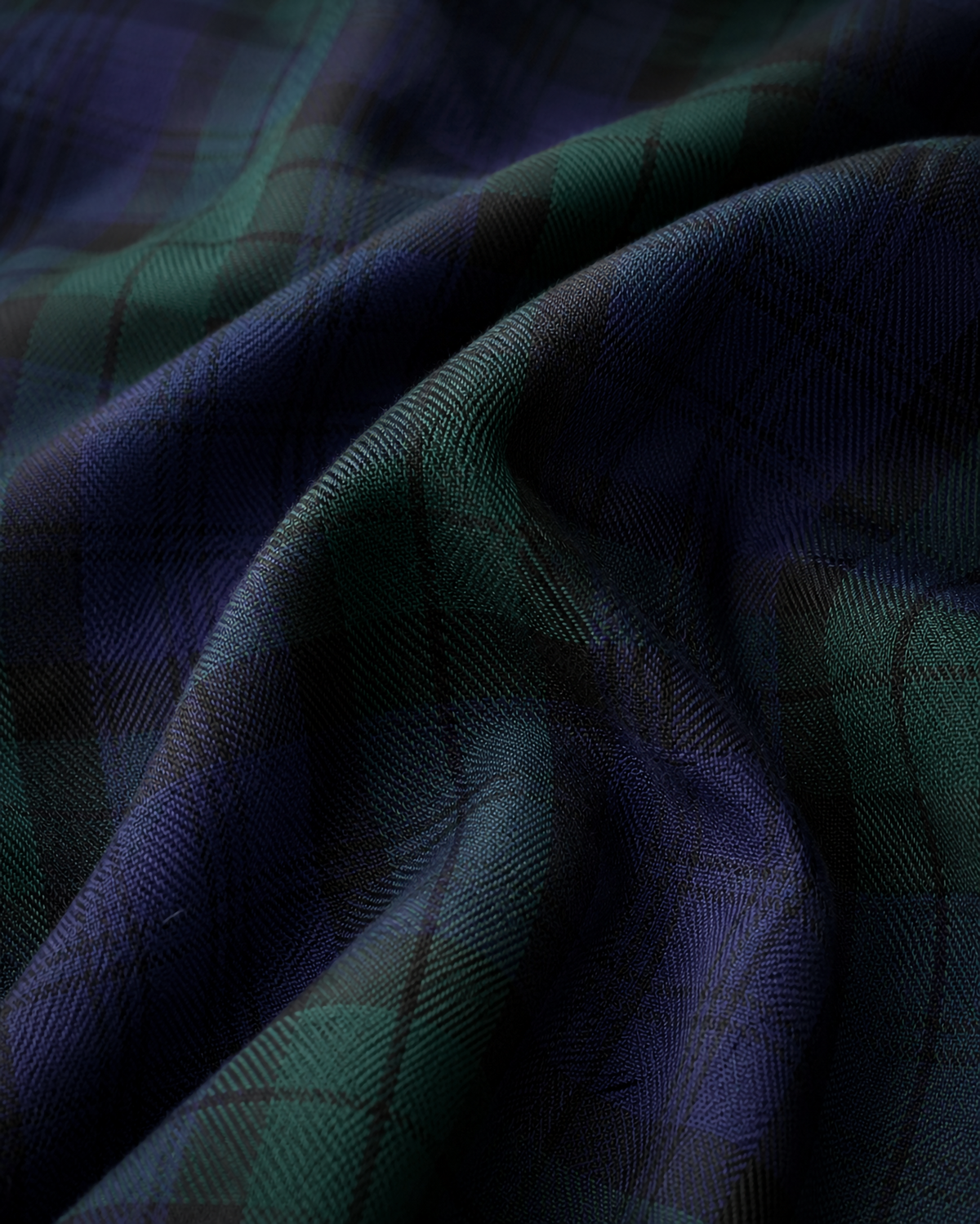 A close-up of draped tartan fabric with a dark green and deep navy blue plaid pattern.