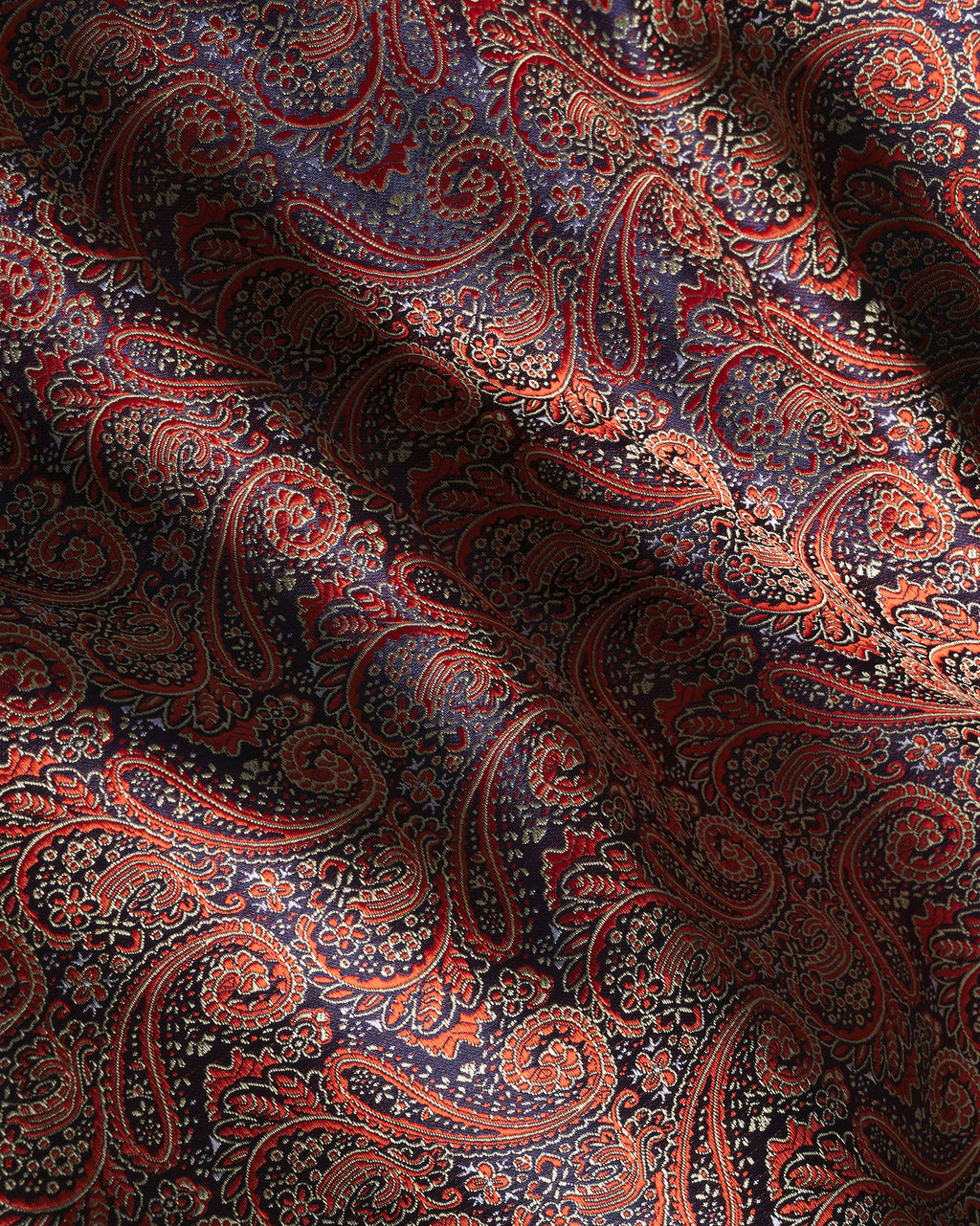 A close-up of draped fabric with an intricate paisley pattern in deep navy blue, red, orange, and beige.